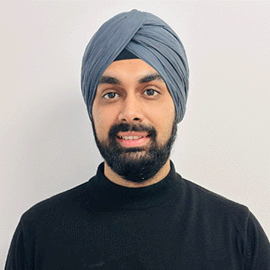 A smiling man wearing a black cardigan in front of a grey background looks directly ahead.